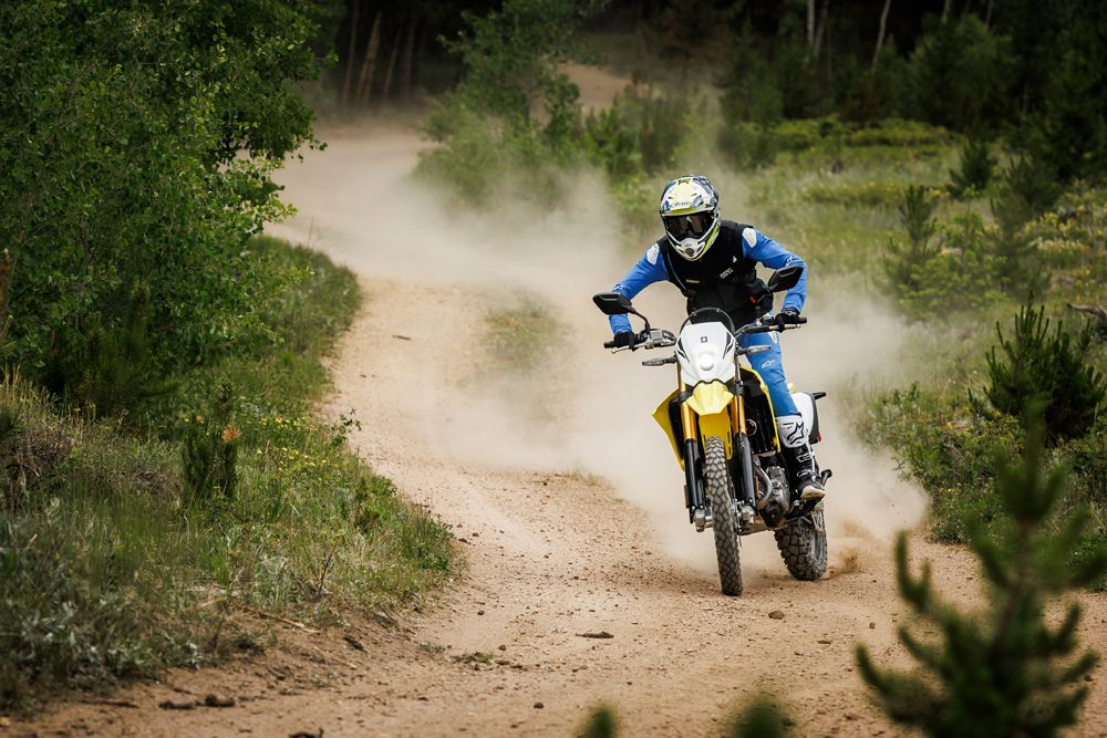 Ein Motorradfahrer fährt auf einem staubigen Waldweg und genießt die Offroad-Abenteuer mit einer gelben Enduro-Maschine.
