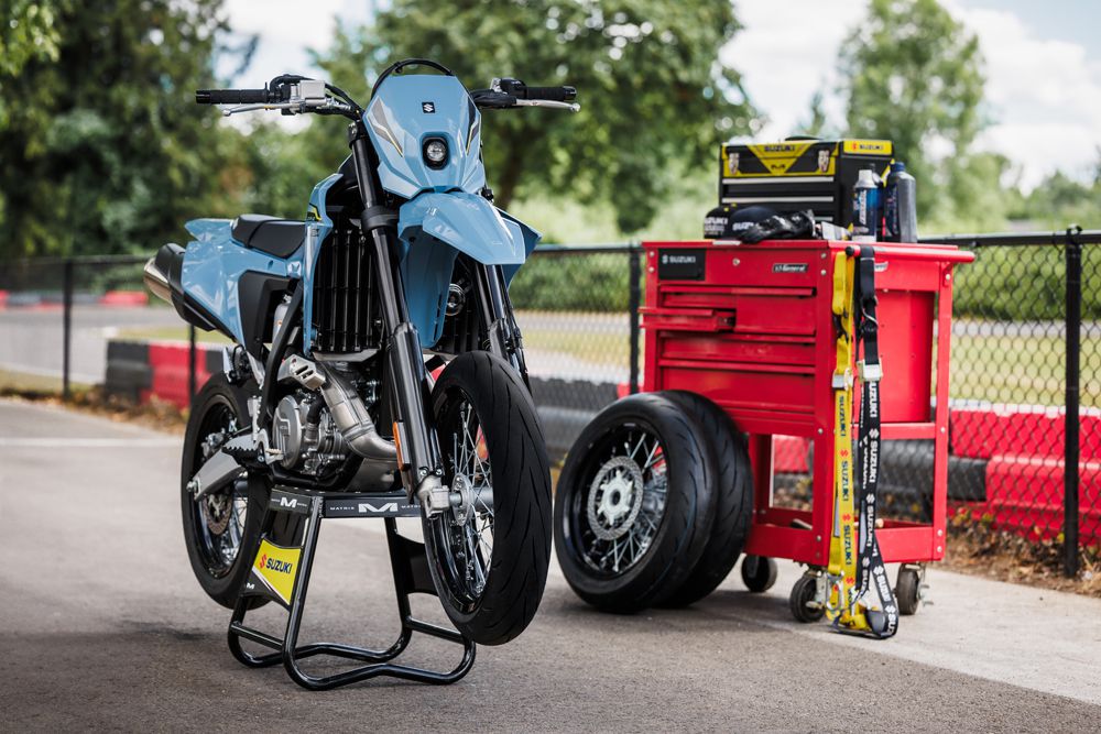Ein hochwertiges Motorrad von Suzuki steht auf einem Ständer neben einer roten Werkbank mit Werkzeug, Reifen und Zubehör.