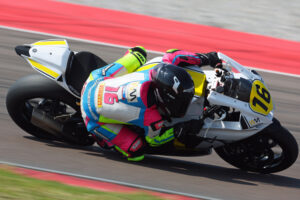 Ein Rennfahrer in auffälliger Motorradbekleidung steuert ein sportliches Motorrad auf einer Rennstrecke.